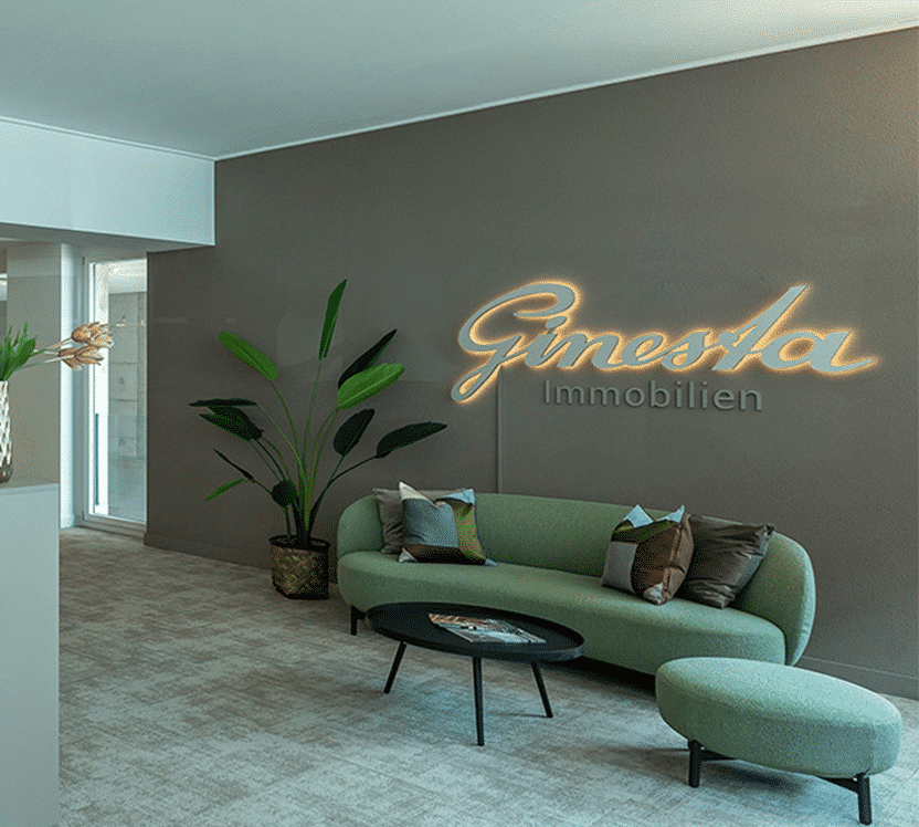Modernes Empfangsbereich von Ginestra Immobilien mit gemütlicher grüner Couch, stilvollem Tisch und Pflanzen, die eine einladende Atmosphäre schaffen. Ideal für die Präsentation von Immobilien.