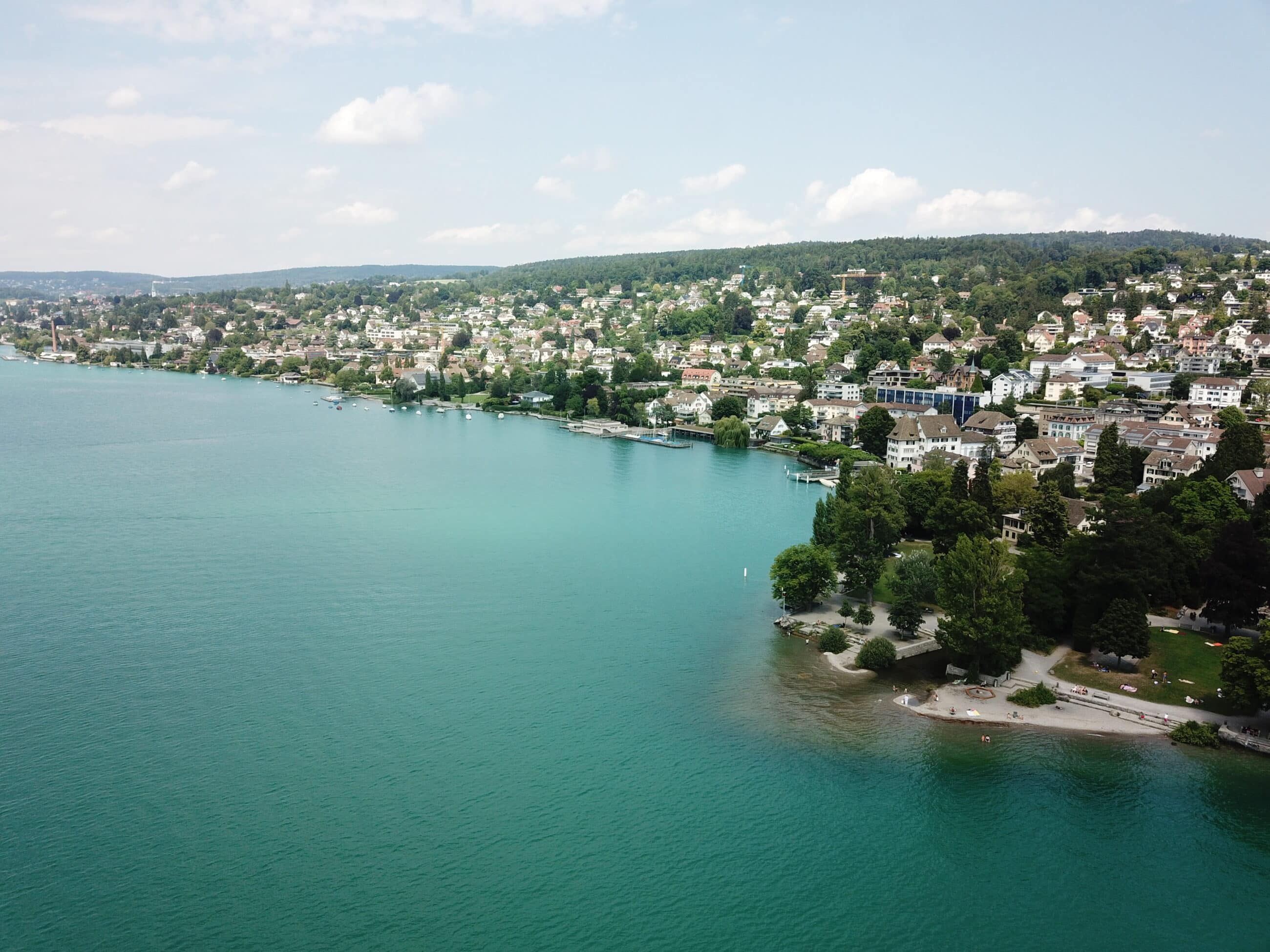 Luftaufnahme einer mediterranen Küstenlandschaft mit sanften Hügeln und klarem blauem Wasser.