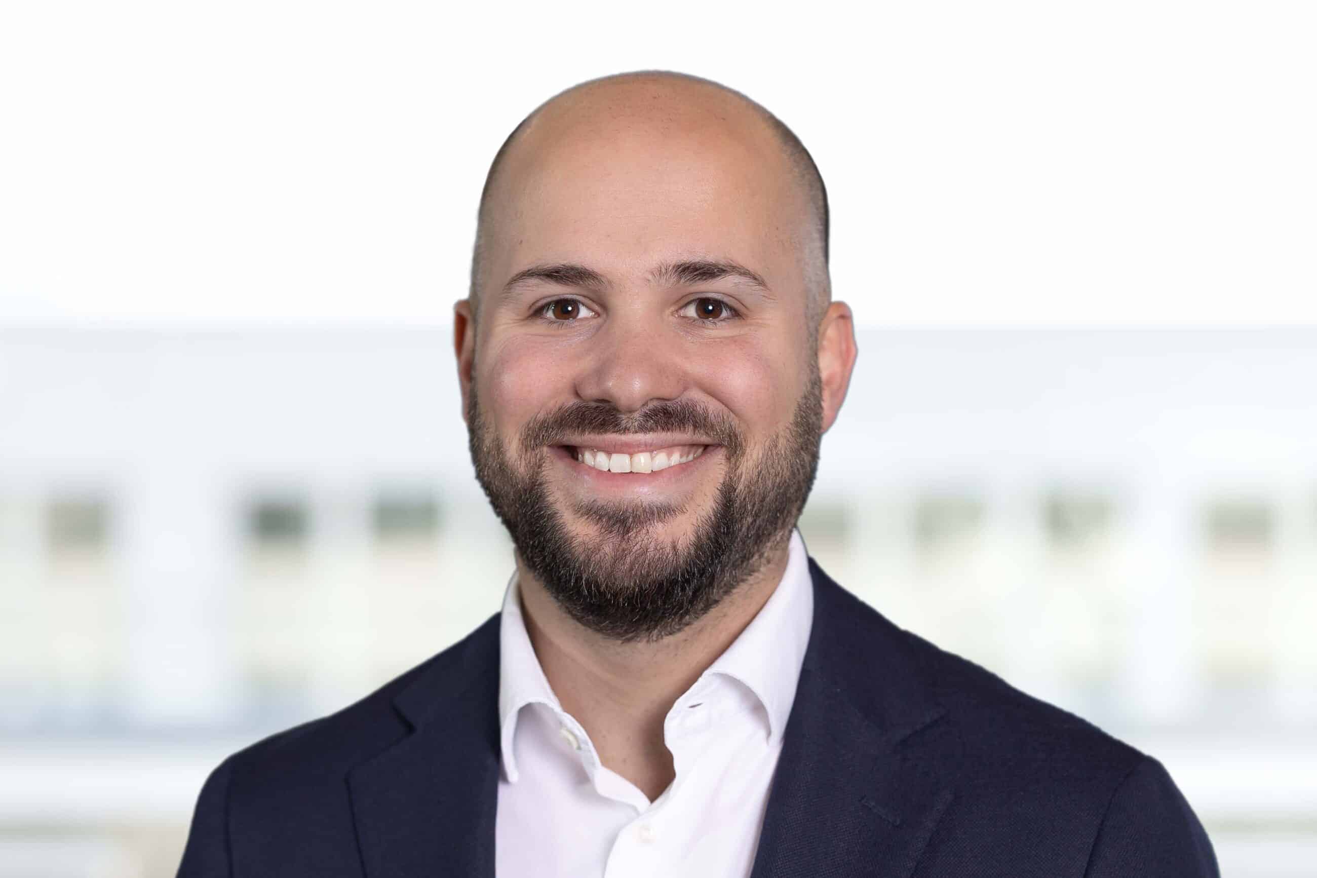 Porträt eines Mannes mit Bart, der lächelnd im Freien steht, umgeben von Natur.