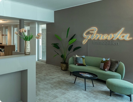 Modernes Immobilienbüro von Ginestra mit stilvollem Empfangsbereich, grünem Sofa und eleganter Dekoration. Die Lichtzeichen Ginestra Immobilien verleihen dem Raum eine einladende Atmosphäre.