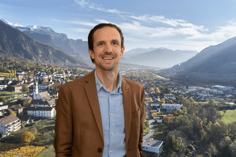 Porträt von Dave, einem jungen Mann mit Brille und lässigem T-Shirt, vor einem urbanen Hintergrund.